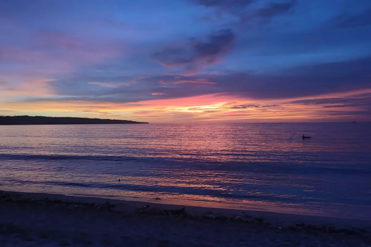 La plage et la baie de Jimbaran au crépuscule, sous un ciel bleu et rose, avec une barque au large