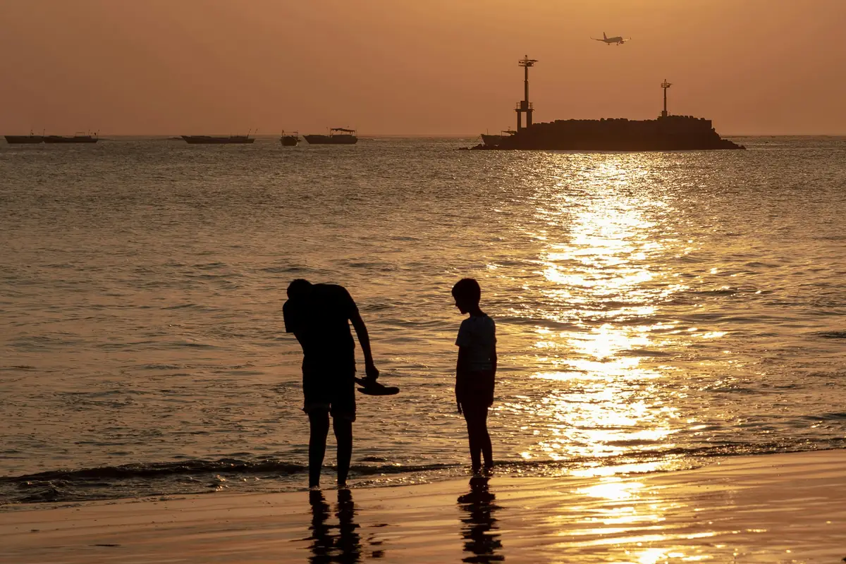 Deux silhouettes à contre-jour au bord de l’eau sur la plage de Jimbaran, dans la lumière dorée du soleil couchant