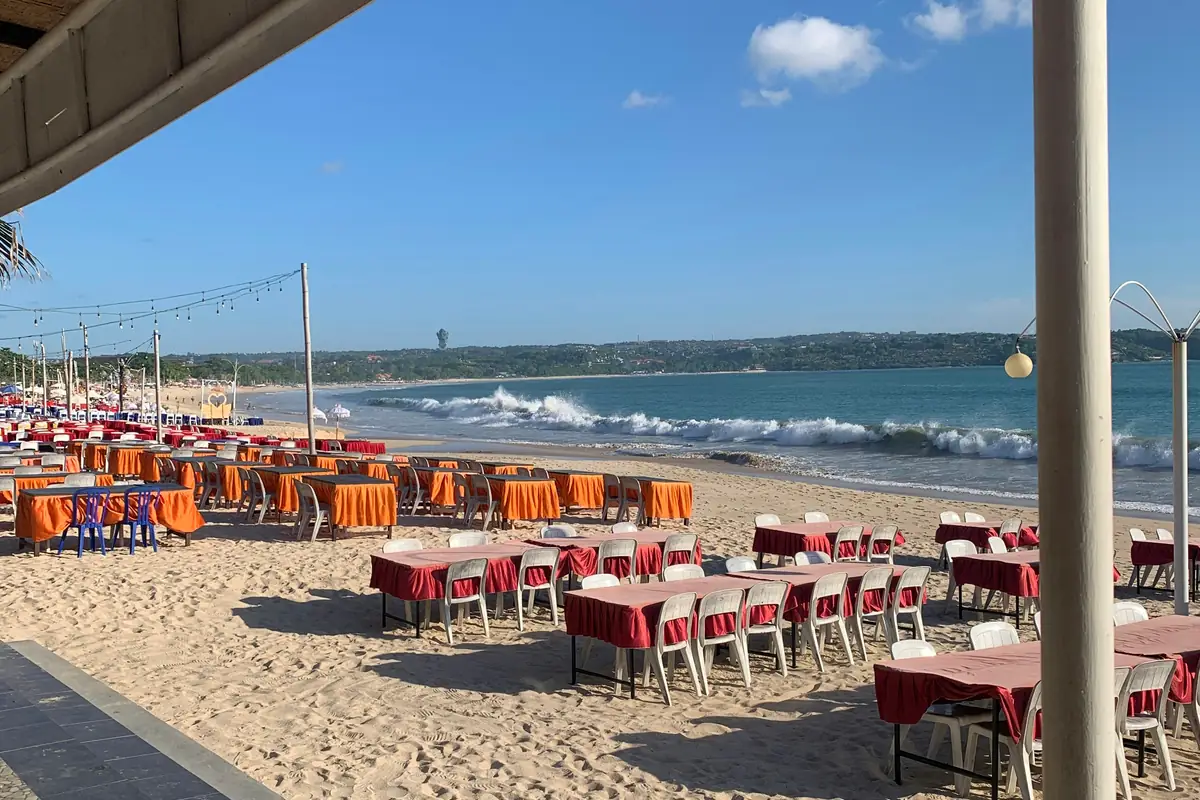 Les tables nappées des restaurants de fruits de mer dressées sur le sable de la plage de Jimbaran, face aux vagues