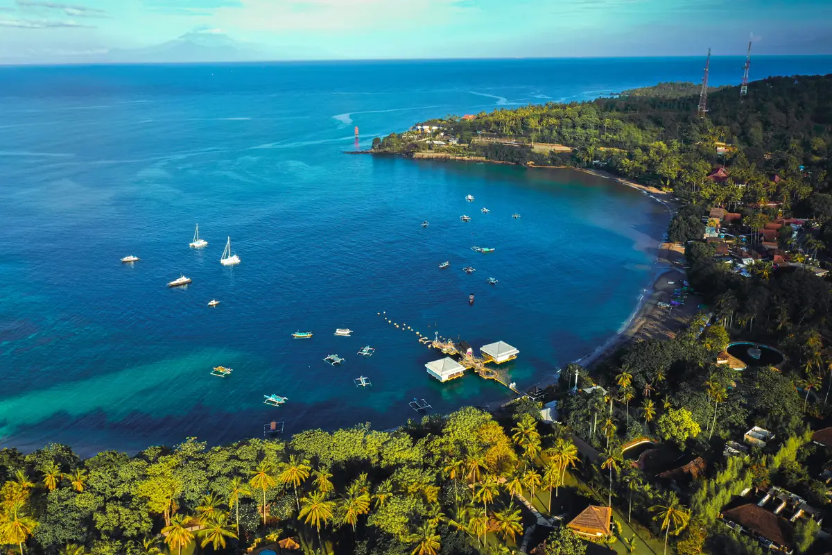 Vue aérienne de la baie de Senggigi à Lombok : eau bleu profond, bateaux au mouillage et cocoteraie