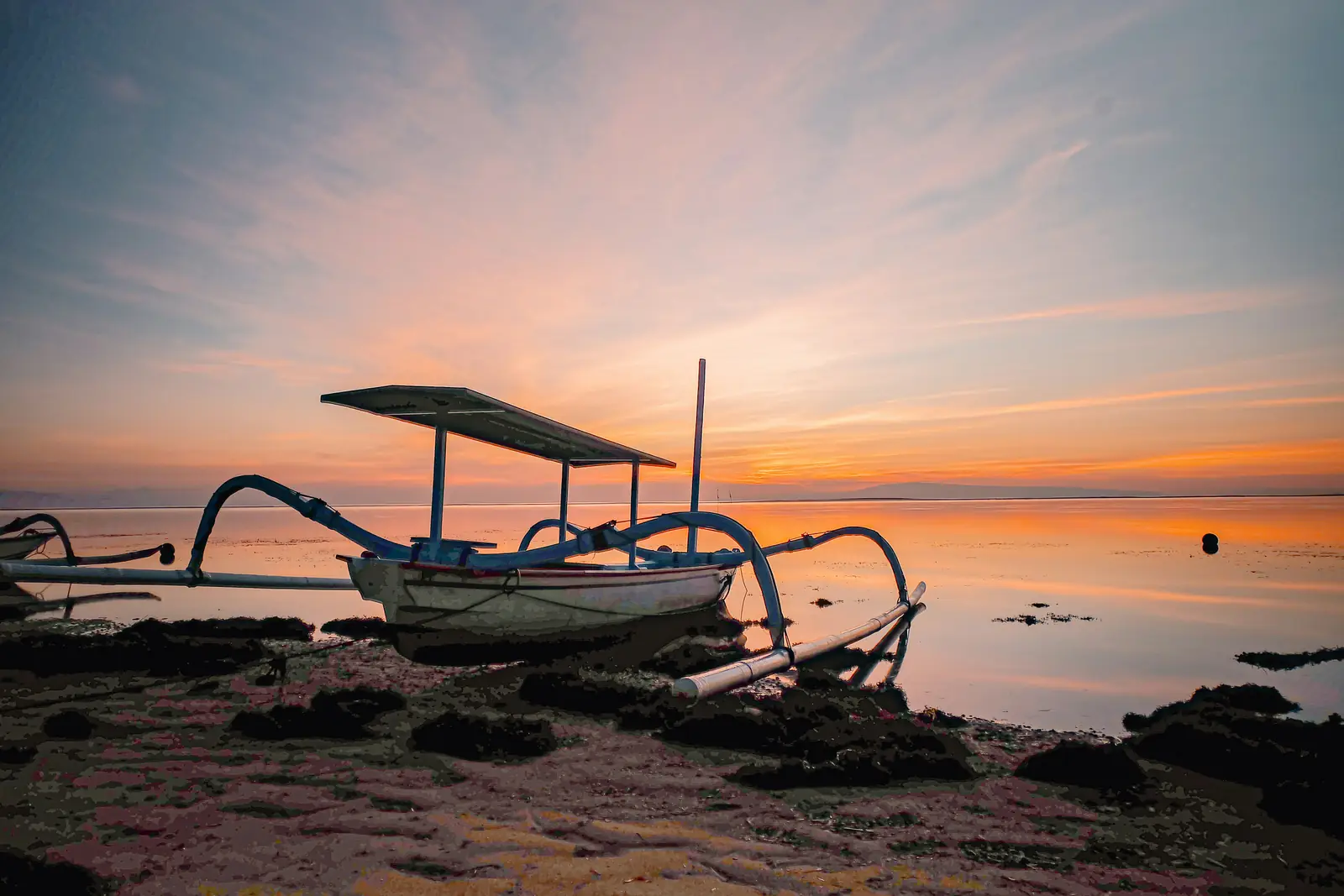 Un jukung, pirogue à balanciers balinaise, échoué sur la plage de Sanur à marée basse sous un ciel rose de lever de soleil