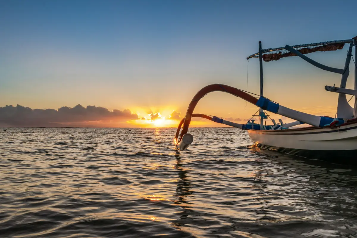 La proue d’un jukung au premier plan et le soleil qui se lève sur la mer à Sanur